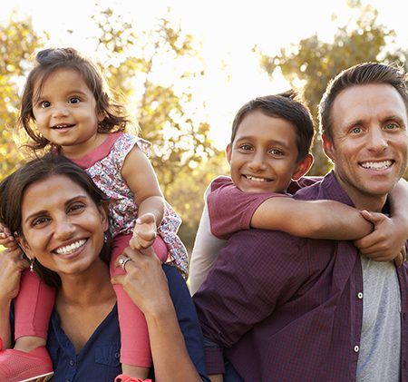Mixed race parents carry their kids piggyback in a park group of parents