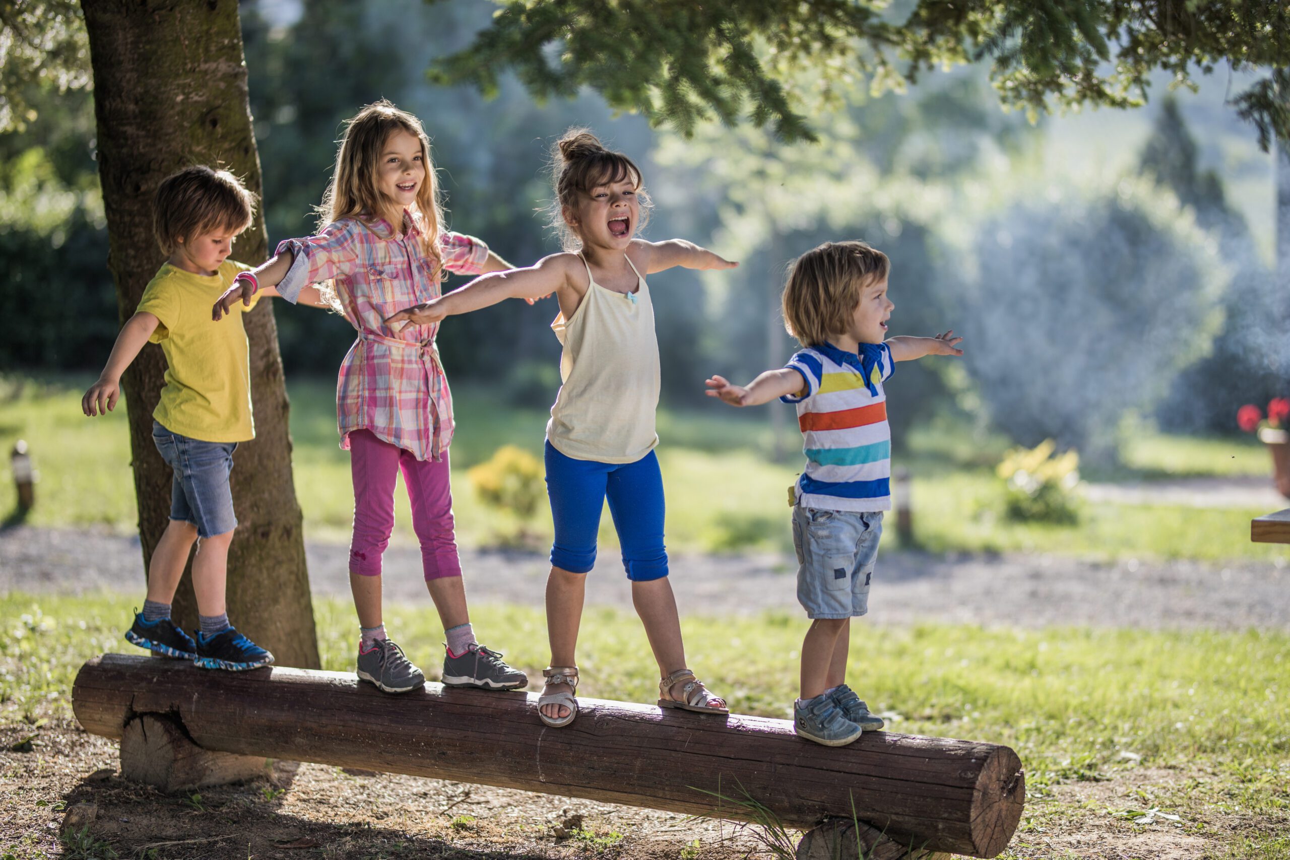 Group of small kids walking on a tree trunk in nature.